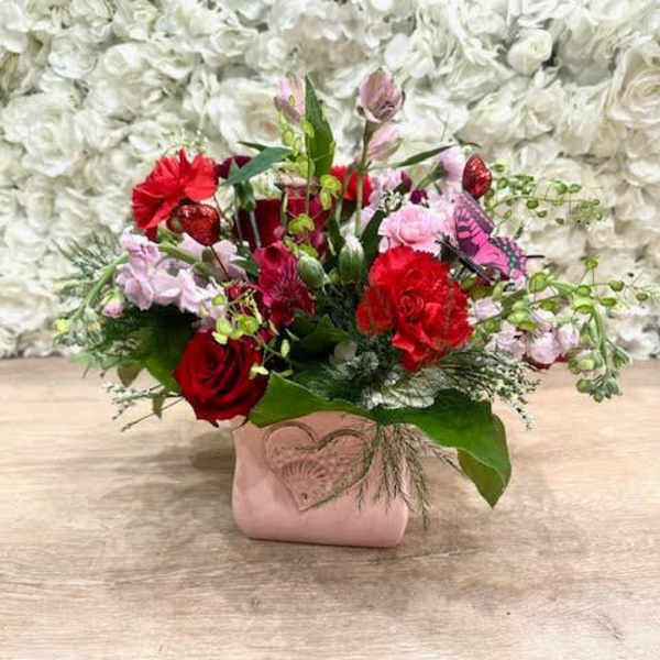 Red and pink mixed flower arrangement in a pink vase with a heart accent