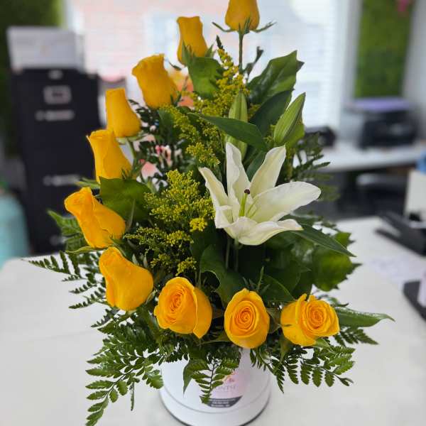 Yellow roses and a white lily arranged in a white vase