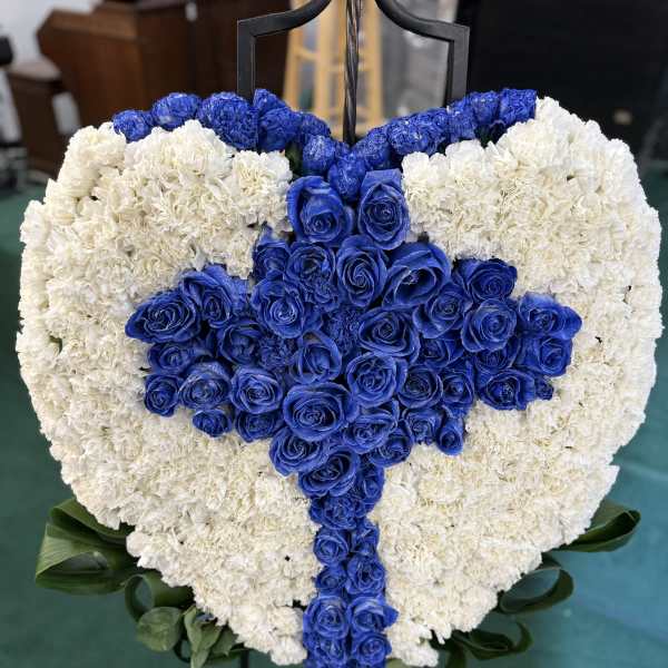 Heart-shaped floral tribute with blue roses and white carnations on an easel