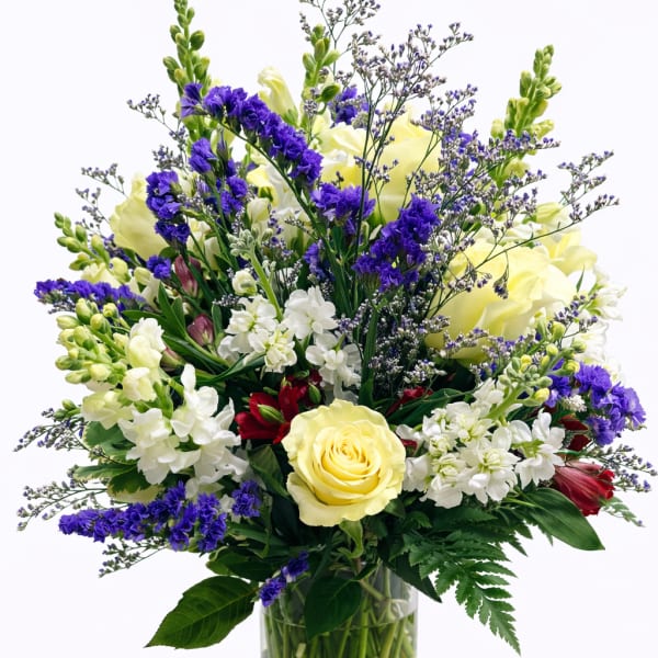 Mixed bouquet of yellow roses, white blooms, and purple flowers in a glass vase