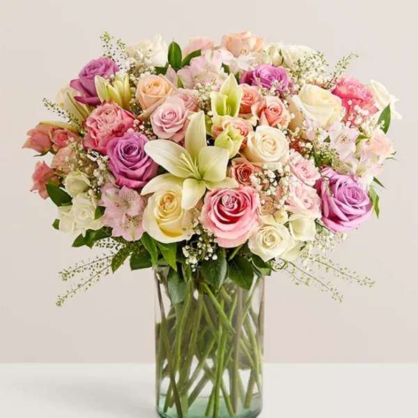 Mixed pastel roses and lilies arranged in a clear glass vase