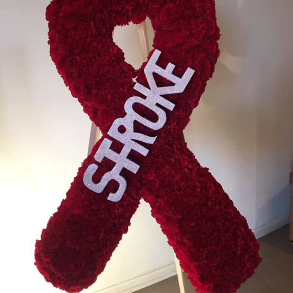 Tall red floral awareness ribbon on a wooden easel with white letters spelling STROKE.