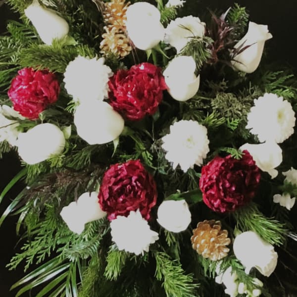 Standing spray with red carnations, white roses, white mums, and pinecones on a metal easel.