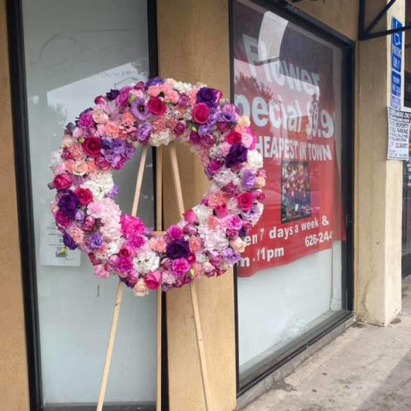 Large pink and purple flower wreath on a wooden easel displayed outside a storefront