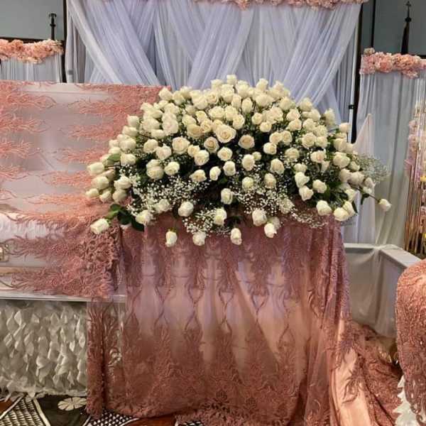 Large arrangement of white roses with baby's breath on a pink lace-covered casket