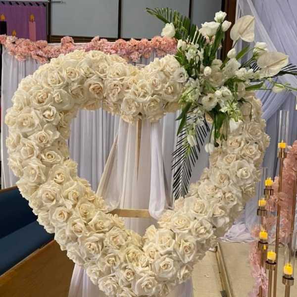 Large heart-shaped wreath of ivory roses on a stand with white accent flowers.