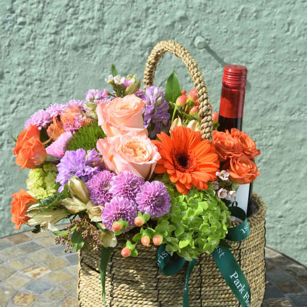 Woven basket of mixed colorful flowers with a wine bottle tucked among the blooms