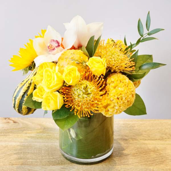 Yellow floral arrangement in a glass vase with white orchids