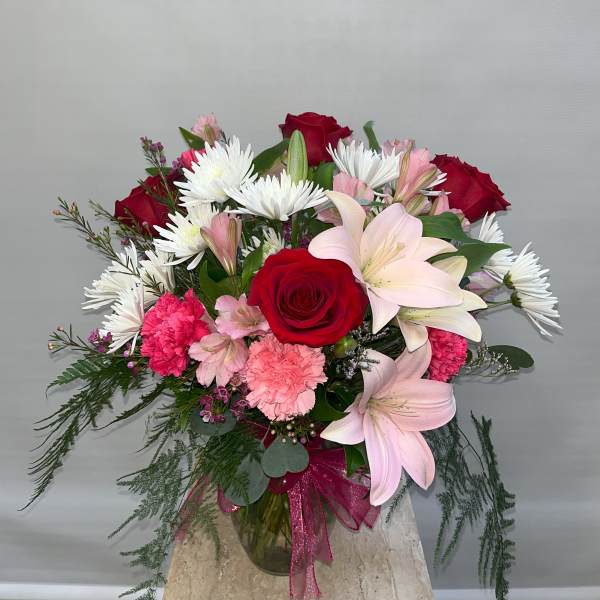 Bouquet of red roses, pink lilies, and white daisies in a glass vase