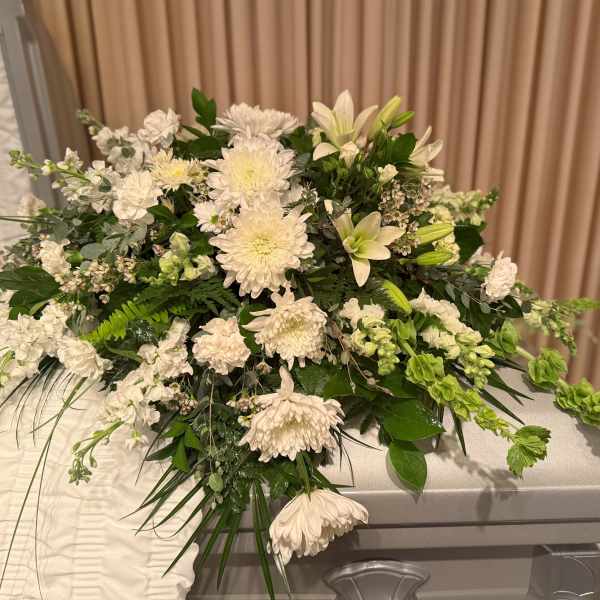 Large white floral spray on a casket with green foliage