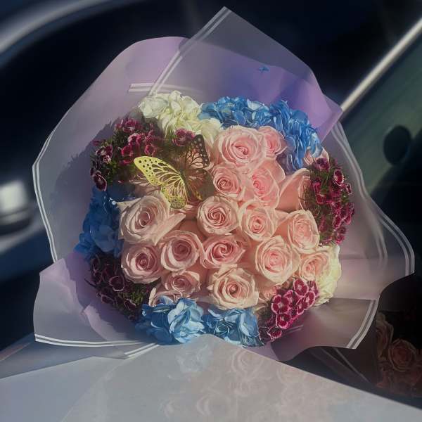 Bouquet of pink roses and blue hydrangeas wrapped in lavender paper