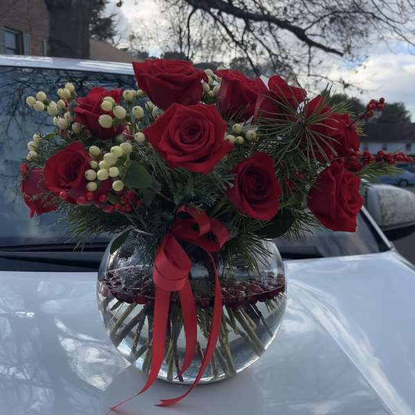 Red roses in a round glass vase with berries and a red ribbon