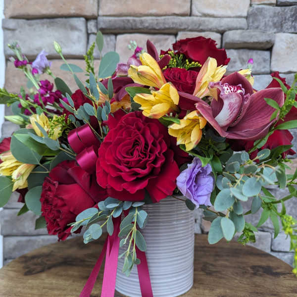 Bouquet of red roses, yellow alstroemeria, and purple flowers in a white vase