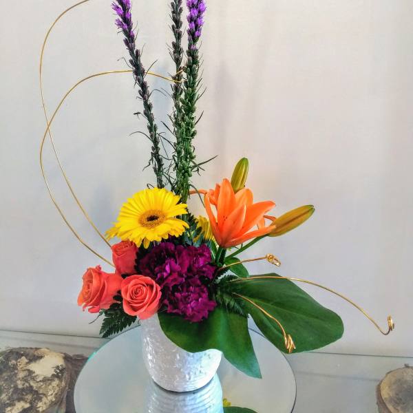 Mixed bouquet with orange lilies, yellow gerbera, and pink roses in a white vase