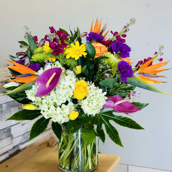 Colorful tropical bouquet in a clear glass vase with orchids and roses