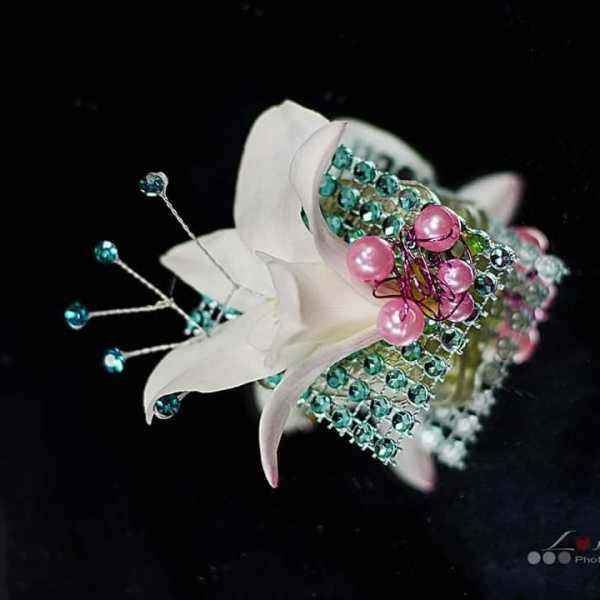 White floral corsage with pink and teal bead accents on a black background