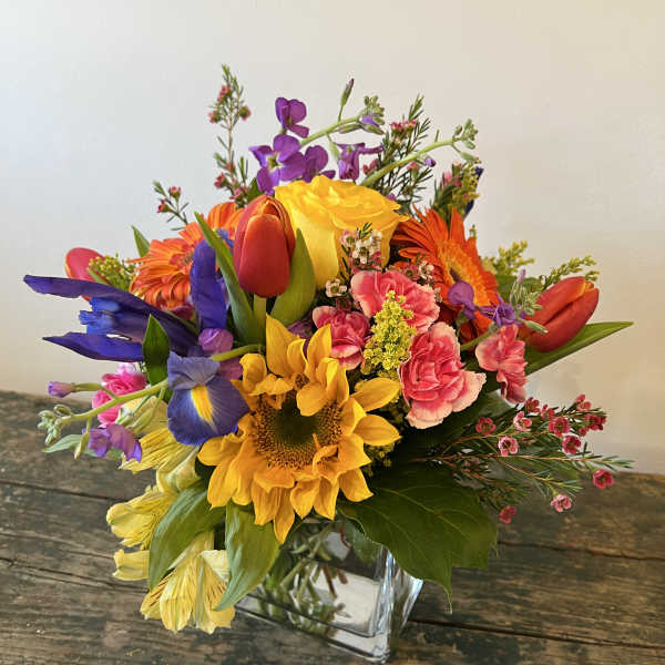 Colorful mixed bouquet in a clear glass vase with sunflowers, tulips, and gerbera daisies