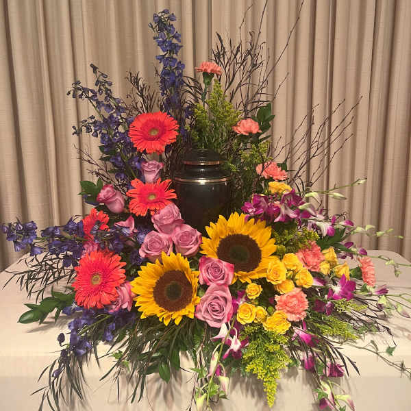 Large floral arrangement with sunflowers, roses, gerberas, and orchids around an urn