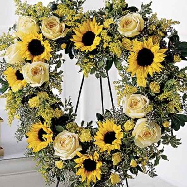 Heart-shaped floral wreath with sunflowers and cream roses on a stand