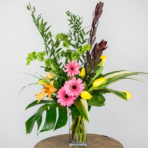Pink gerbera daisies with yellow tulips and orange lilies in a glass vase