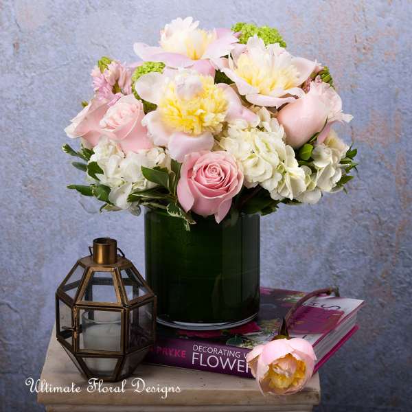 Pink and white flower arrangement in a dark green vase with a lantern beside it