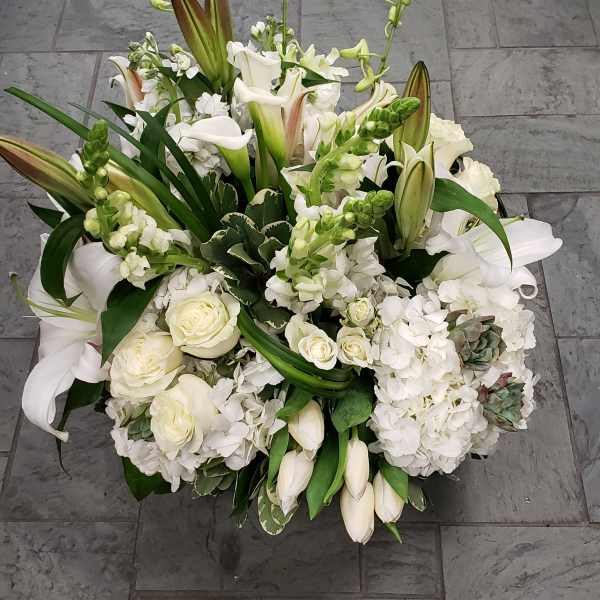 White floral arrangement with lilies, roses, and calla lilies in a low design