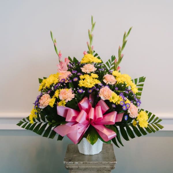 Colorful floral arrangement in a white vase with a pink bow