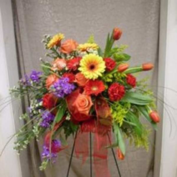 Colorful mixed flower arrangement on a black stand with a sheer ribbon