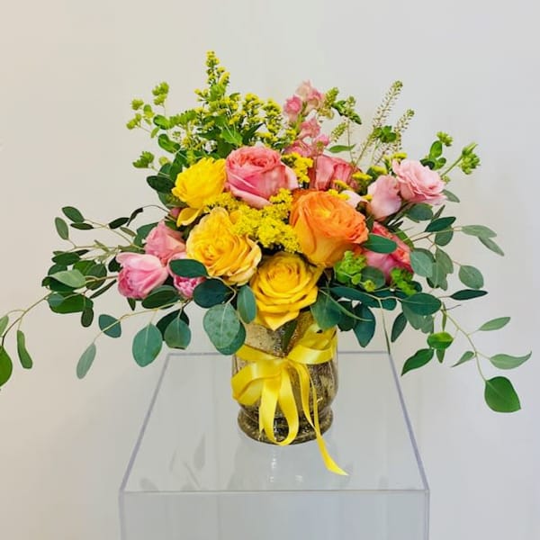 Bouquet of pink and yellow roses in a glass vase with a yellow ribbon