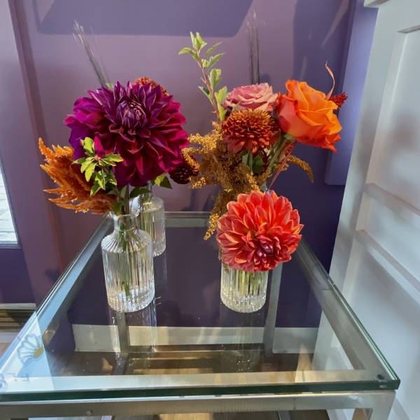 Three small floral arrangements in clear glass vases on a glass table