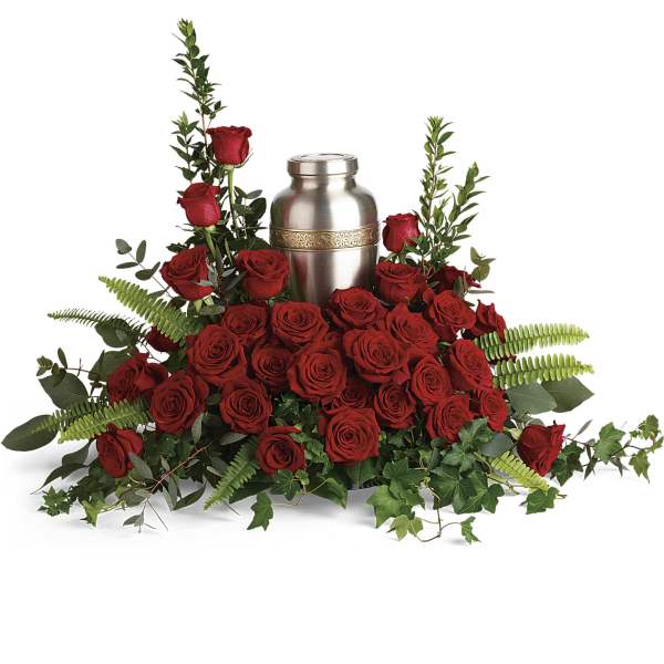 Red rose cremation arrangement surrounding a silver urn with ferns and trailing ivy