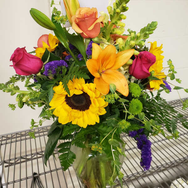 Mixed bouquet with sunflowers, roses, lilies, and snapdragons in a glass vase