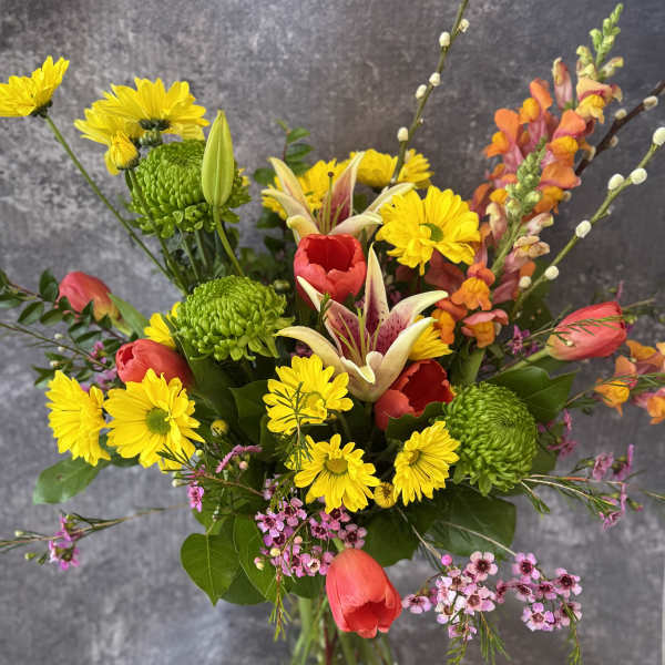 Mixed bouquet of yellow daisies, red tulips, and lilies in a glass vase