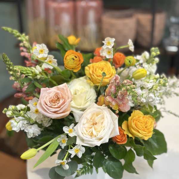 Mixed arrangement of yellow, peach, and white roses with spring blooms in a white vase