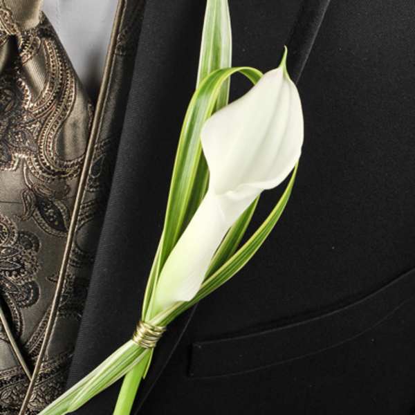 White calla lily boutonniere with striped greenery on a black suit lapel and patterned gold vest.