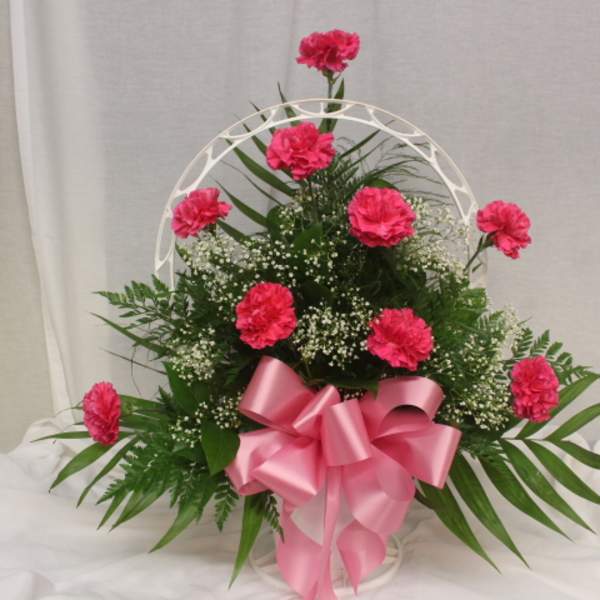 Pink carnation arrangement with a large pink bow in a white basket