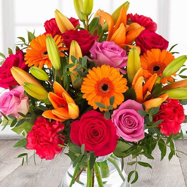 Mixed bouquet of roses, lilies, gerbera daisies, and carnations in a glass vase