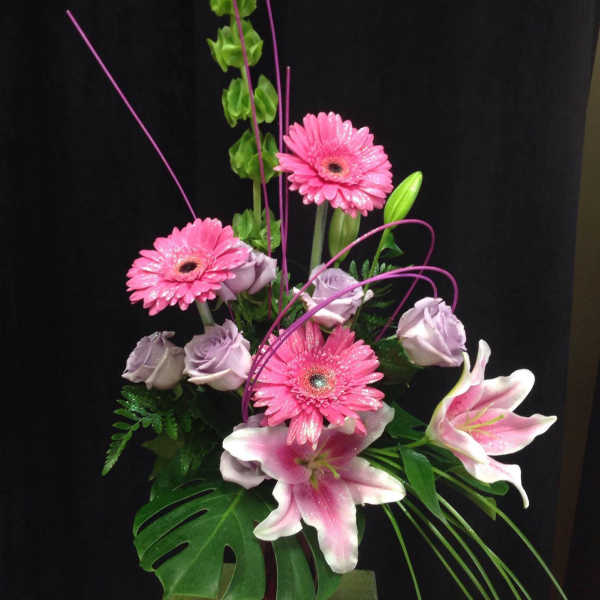 Pink gerberas and lilies arranged in a vase with lavender roses