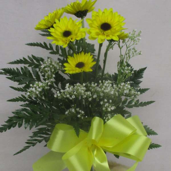 Yellow daisy bouquet in a glass vase with a teddy bear