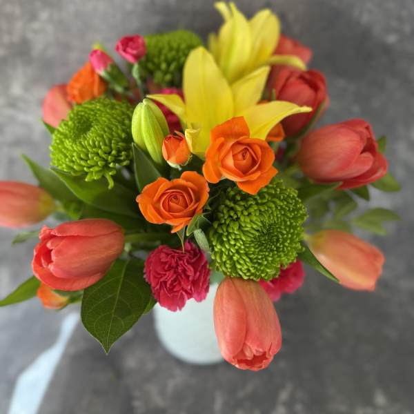 Bouquet of orange roses, yellow lilies, and pink tulips in a white vase