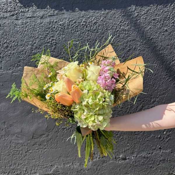 Hand-tied bouquet with green hydrangeas, cream roses, peach tulips and pink blooms in kraft paper wrap