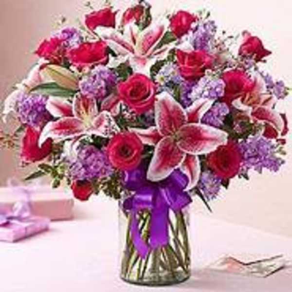 Pink roses and lilies arranged in a glass vase with a purple ribbon
