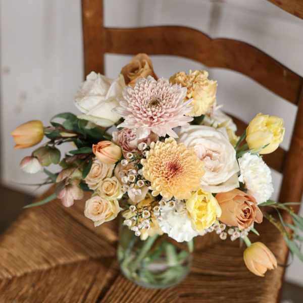Mixed pastel bouquet in a glass vase on a wooden chair