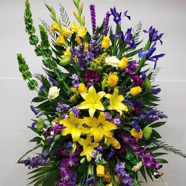 Tall standing spray of yellow lilies, roses, and purple blooms on a metal easel