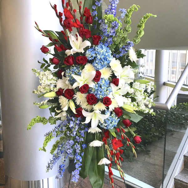 Tall red, white, and blue standing spray with roses, lilies, hydrangeas, and delphinium on an easel stand