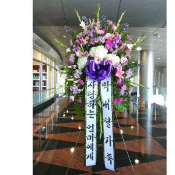 Tall standing spray of pink, purple, and white flowers with ribbons and a purple bow on an easel