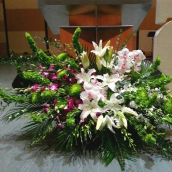 Large white lily and orchid floor arrangement with green accents in front of a stage