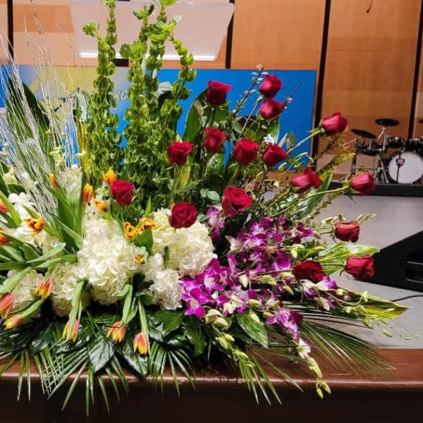 Large mixed floral spray with red roses, white hydrangeas, yellow-red tulips, and purple orchids.