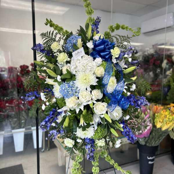 Large blue and white funeral spray on an easel with ribbon