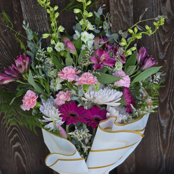 Hand-tied bouquet of pink and white flowers wrapped in white paper with a pink bow.